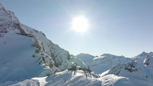 Vue aérienne de touristes debout près de la falaise d'une montagne enneigée sous le soleil