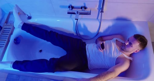 Man Lying in Bathtub with Clothes and Socks