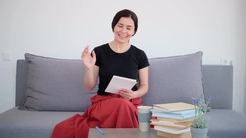 Woman Smiling and Waving While Sitting on Couch