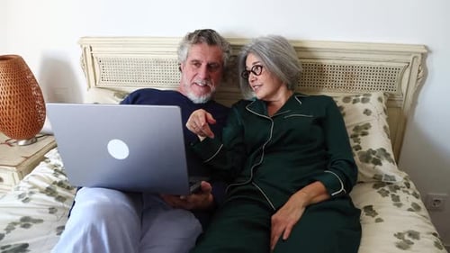 Senior Couple in Pajamas Using Laptop in Bed