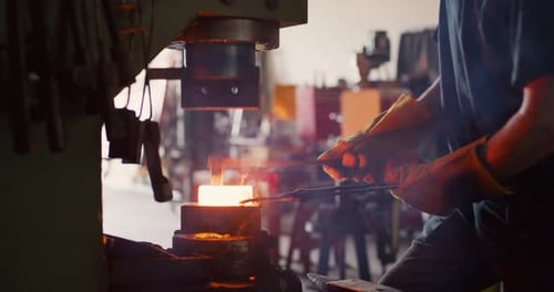 Professional blacksmith walks to press red hot iron in workshop