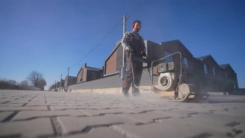 Construction Worker Using Plate Compactor on Brick Road