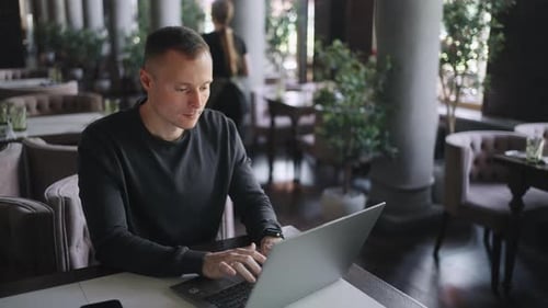 WebDeveloper And IT Professional Man Working Remotely Sitting With Laptop In City Cafe Portrait