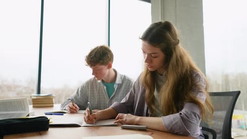 Students Writing at Desk in Sunlight Classroom