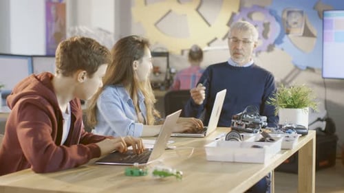 Dans un cours d'informatique, un professeur explique la mécanique à un jeune garçon et à une jeune fille, ils prennent des notes en utilisant