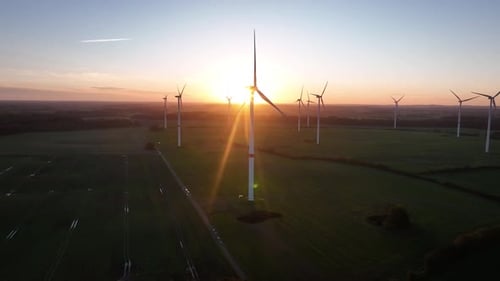 Aerial footage of large spinning wind turbine within a wind farm in agricultural fields captures the