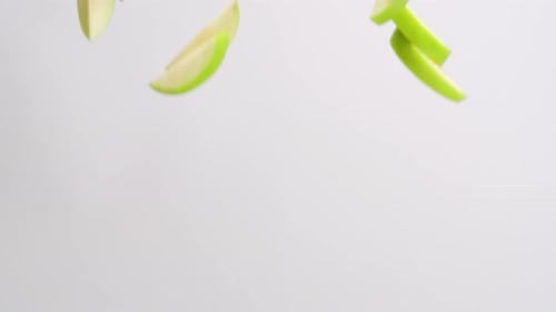 Fresh green apple slices spinning and falling on white backdrop in slow motion