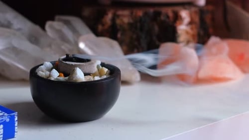 Close up shot of burning incense with white smoke in a bowl with crystal gemstones in the background