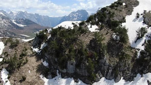 Vue par drone en Albanie dans les Alpes survolant un sommet enneigé et rocheux Vue rapprochée à Theth