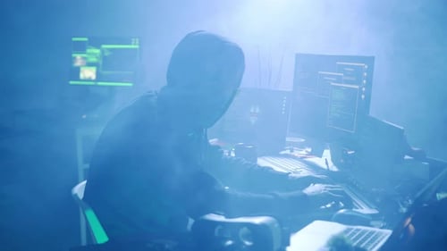 Un misterioso y esquivo hacker opera en una habitación con poca luz rodeada de múltiples pantallas