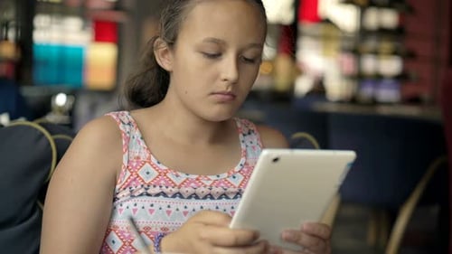 Teenage girl happily browsing the internet on her tablet in a cozy cafe