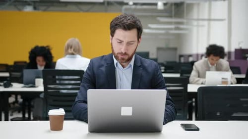 Portrait d'un bourreau de travail en train de taper sur son ordinateur portable pendant que ses collègues travaillent derrière