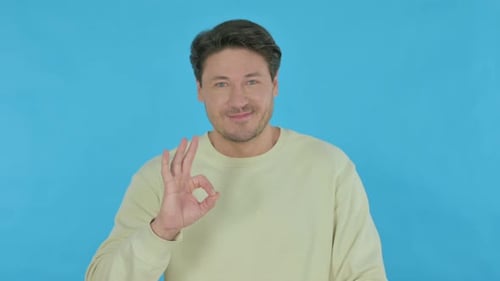 Man Gives Okay Gesture in Front of Blue Background