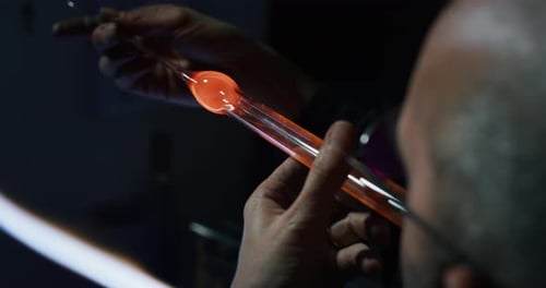 Slow motion of experienced glass blower working with flame on a handmade art piece of glass from p