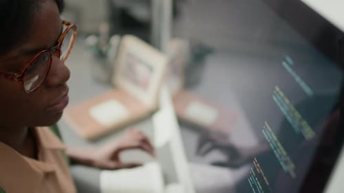 Nahaufnahme einer Afroamerikanerin mit Brille, die im Büro Code schreibt