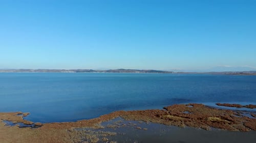 Peaceful blue lagoon with shallow clear water reflecting bright clear sky, dry grass and reeds on sh