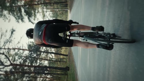 Cyclist riding bicycle out of saddle, hard pushing pedals. Vertical video