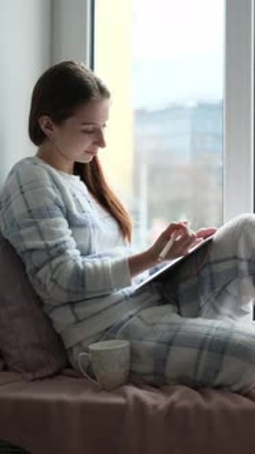 Teenage Girl Sitting On Windowsill Writing Notes In Notebook