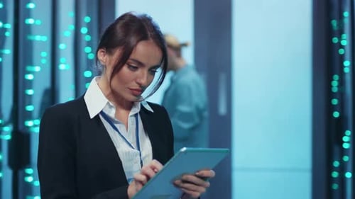 A Skilled Woman Uses a Tablet in a Server Room Managing Servers