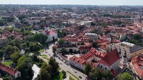Drone advances above Vilnius Old Town, revealing traffic, rooftops, and church tower.