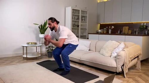 Hombre haciendo sentadillas laterales, tutorial de observación de ejercicios en la computadora en casa
