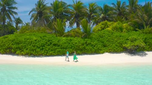 Beautiful Traveler Couple Walks Down a Tropical Beach with Turquoise Sea and Sunshine in the