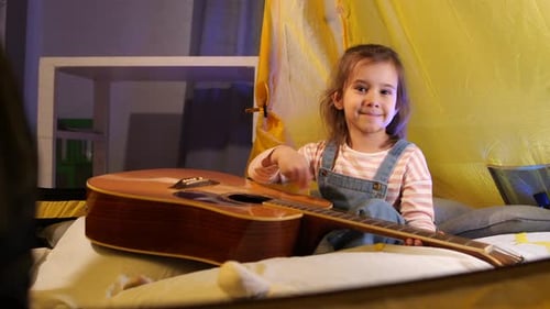 Smiling Girl Strums Guitar in Cozy Indoor Tent