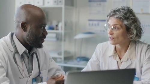 Doctors Discussing Patients Information on Laptop at Desk in Medical Office