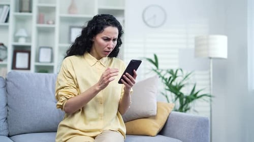 Woman Frustrated Using Smartphone on Sofa at Home
