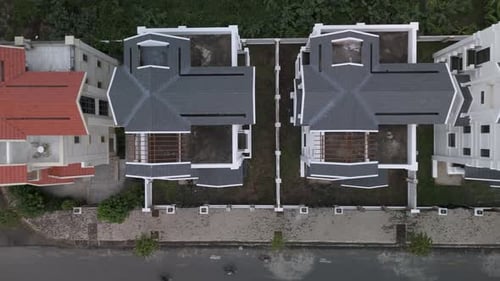 A newly constructed row of identical large white multi story villa styled houses along a road.