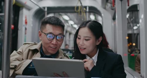 Lovely Asian Couple Sitting Close in Moving Train Man Showing Something to Girl on Tablet Screen