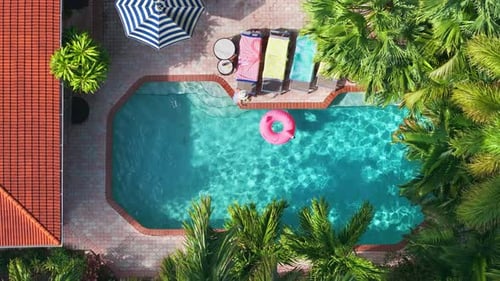 Aerial View of Woman Sunbathing on Lounger Beside Sparkling Tropical Pool