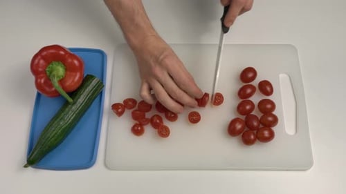 Mann schneidet Pflaumentomaten mit einem Messer. Ansicht von oben nach unten. Hobbykoch