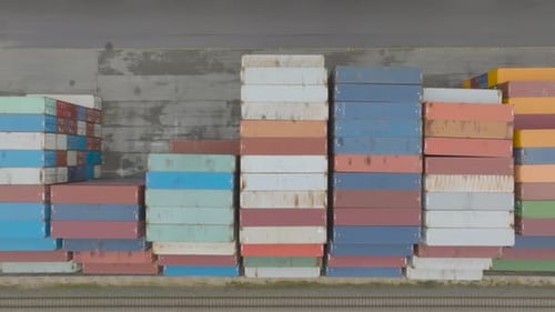 Blick von oben auf viele leere, verrostete und farbige Seecontainer aus Metall, die in einem Hafenterminal aufgereiht sind.
Weltweit