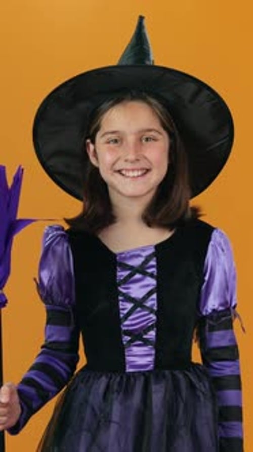 Smiling Girl in Witch Costume Against Orange Backdrop