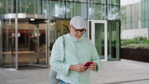 Elegant Relaxed Middle Aged Man Using Cell Phone App Outside the Office Building