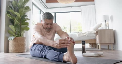 Mature Man Stretching Legs in Bedroom on Yoga Mat