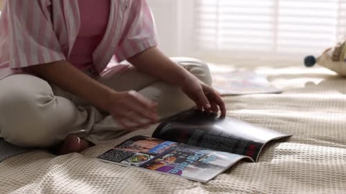 Woman reading lifestyle magazine on bed at home, closeup. Camera moving forward