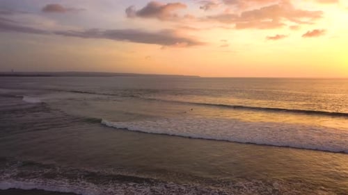 Drone video of surfers, riding a wave at the beach in Canggu, Bali, Indonesia at sunset, flying forw