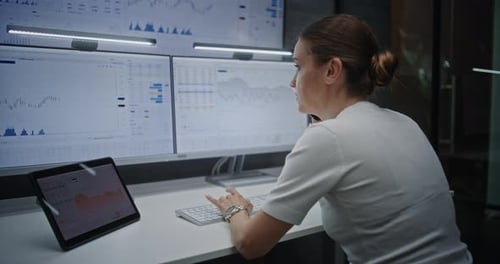 Female Financial Analyst Having Phone Call Analyzing RealTime Stocks on MultiMonitor Computer