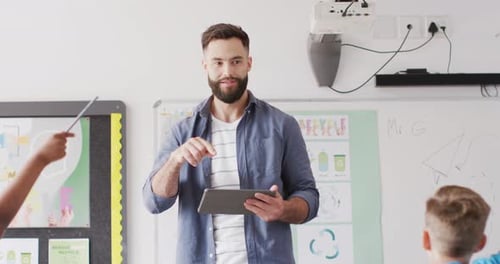 Diverse male teacher and happy schoolchildren at desk in school classroom