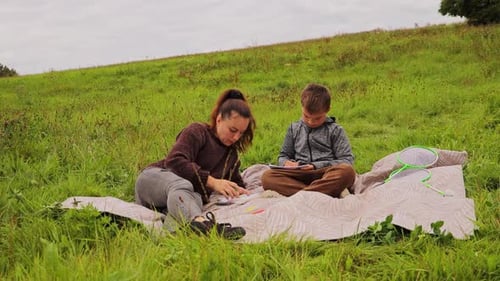 A mother and her young child are sitting on a blanket in a grassy field