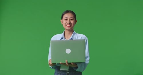 An Asian Woman Using Laptop Computer And Smiling To Camera On Green Screen Background