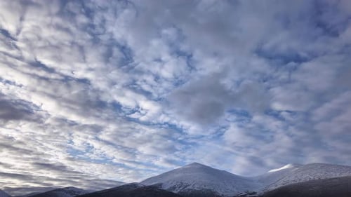 Observe the captivating transformation of the sky as clouds drift gracefully over majestic, snow-cov