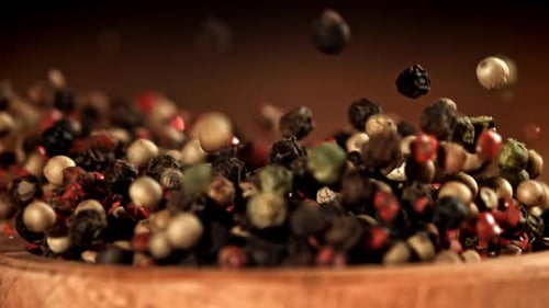 Colorful peppercorns falling into wooden bowl in slow motion