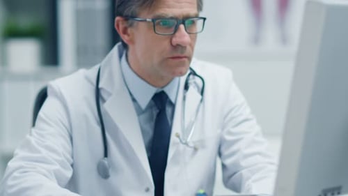 Close-up of a Male Senior Doctor Working at His Desk on a Personal Computer. Reflection of the Scre
