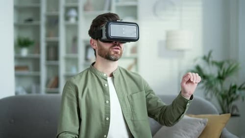 Man works using VR glasses in virtual reality simulator sitting on sofa in living room at home