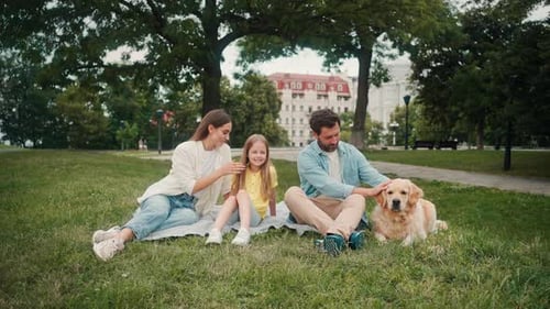 Positive Family with Dog Sits on Mat on Grass Lawn of Park