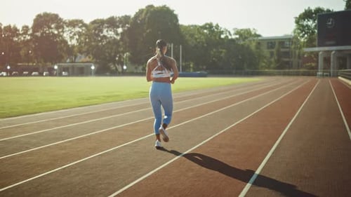 Beautiful Fitness Girl in Light Blue Athletic Top and Leggings Jogging in the Stadium. She is Runni
