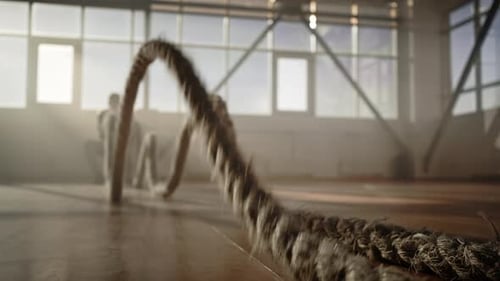 Selektiver Fokus auf Kampfseile, die sich wie Wellen bewegen, wenn ein entschlossener Athlet im Fitnessstudio ein Ausdauertraining durchführt